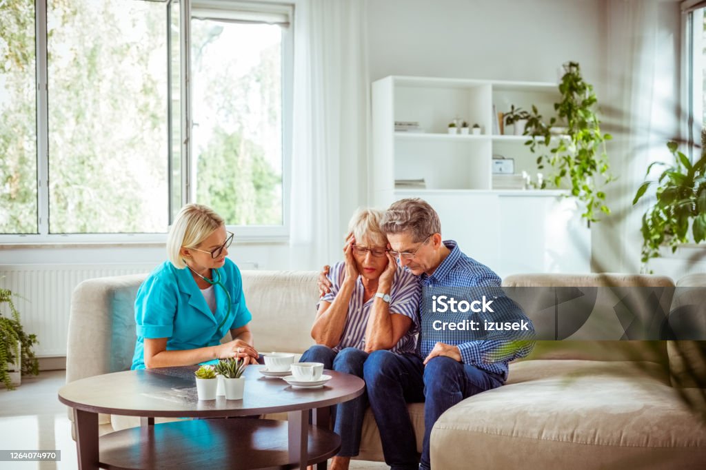 Nurse talking with worried senior couple Worried senior woman feeling unwell, getting bad news. Senior man consoling her. They are sitting with nurse in hospital waiting room. Bad News Stock Photo