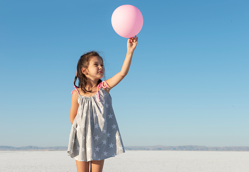 Girl holding pink balloon in salt lake.