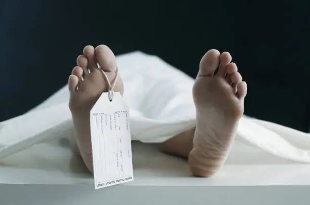 Toe tag hanging on woman lying on table in morgue