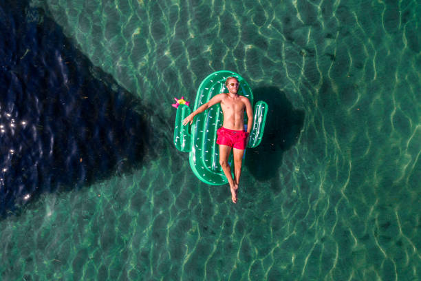 vista aérea do homem flutuando no lago com tochas infláveis de cacto - inner tube swimming lake water - fotografias e filmes do acervo