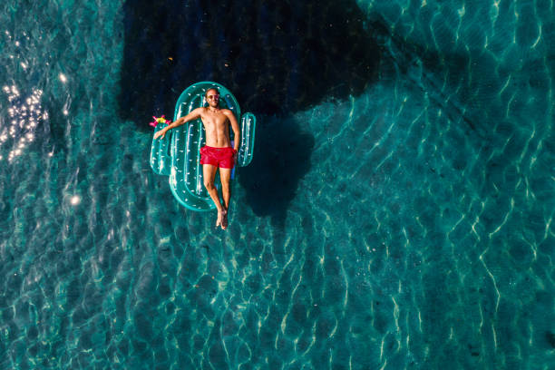Aerial view of man floating on lake with inflatable cactus sunbathing Drone view of one man relaxing on inflatable mattress floating on water stock pictures, royalty-free photos & images