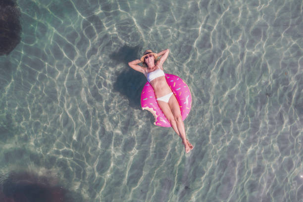 vista aérea de mulher flutuando em lago com colchão inflável tomando sol - inner tube swimming lake water - fotografias e filmes do acervo