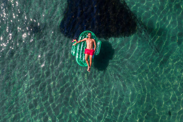 vista aérea do homem flutuando no lago com tochas infláveis de cacto - inner tube swimming lake water - fotografias e filmes do acervo