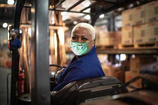 Retrato de una trabajadora que conduce carretilla elevadora en el almacén - usando máscara facial photo