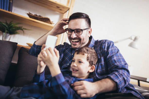 istock Father and little son sitting on couch at home using smart phone 1264076612