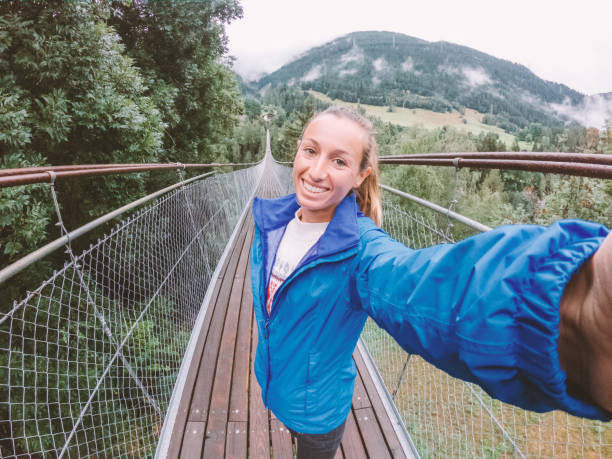 istock Woman takes selfie on suspension bridge crossing over pine tree valley 1264078310