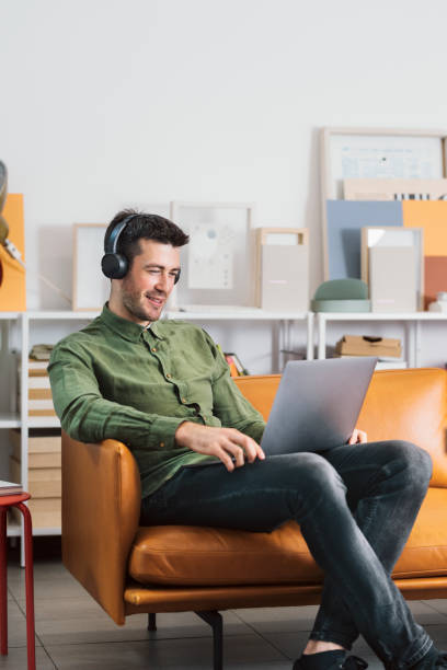 Modern Working Stations: a Smiling Freelancer Sitting in the Office with Headphones on and Listening to Music While Working on his Laptop PC