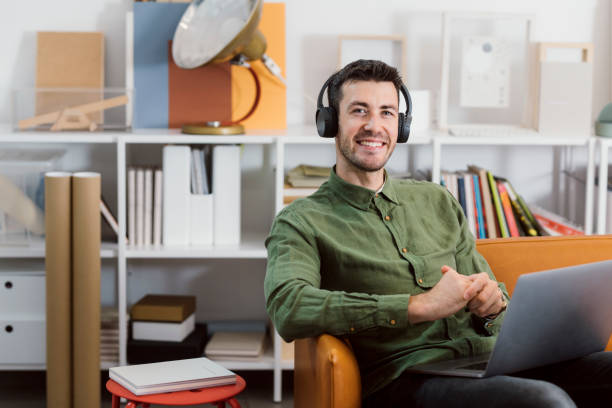 istock Modern Working Stations: a Smiling Freelancer Sitting in the Office with Headphones on and Listening to Music While Working on his Laptop PC 1264090903