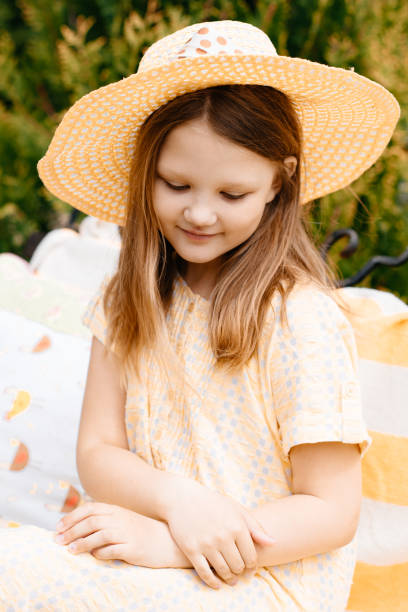 istock A shy girl in a straw hat sits on a bench. 1264092303