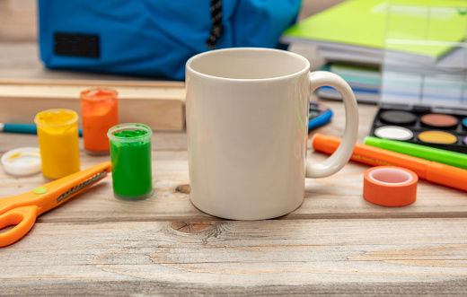 Milk cup white, blank and school supplies on wooden desk background. Beverage for children breakfast in the morning at home or while studying homework, kid tea or hot chocolate break.