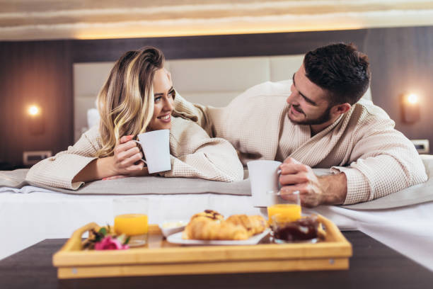 ホテルの部屋でベッドで朝食をとっている笑顔のカップル - honeymoon hotel hotel suite hotel room ストックフォトと画像