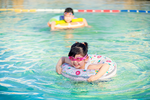 Little girl in swimming pool with inflatable toy ring. Kids swim on summer vacation.