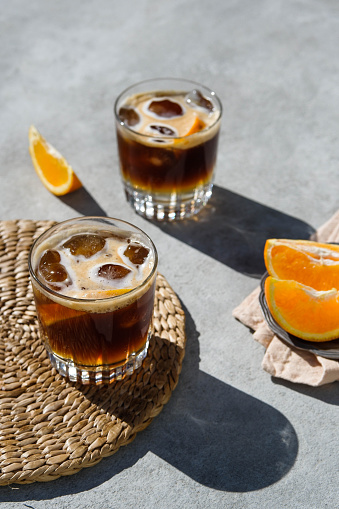 Cold coffee drink for hot summer days — the way to make it step by step. The ingredients and props are: cool glasses, an orange, ice cubes, tonic water and shots of espresso. Shot with natural hard light