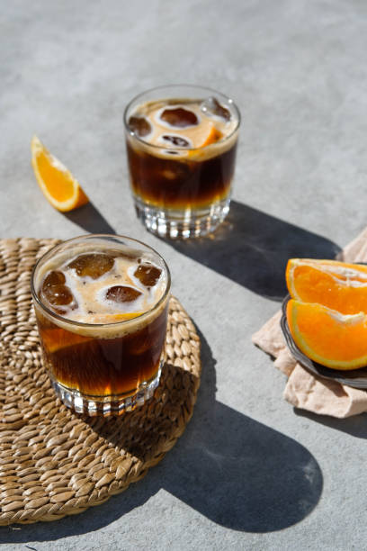 Espresso tonic preparation Cold coffee drink for hot summer days — the way to make it step by step. The ingredients and props are: cool glasses, an orange, ice cubes, tonic water and shots of espresso. Shot with natural hard light tonic water stock pictures, royalty-free photos & images