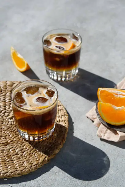 Cold coffee drink for hot summer days — the way to make it step by step. The ingredients and props are: cool glasses, an orange, ice cubes, tonic water and shots of espresso. Shot with natural hard light