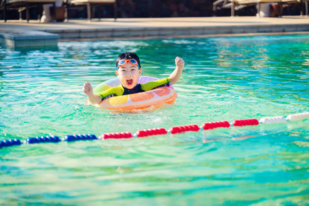 Little boy in swimming pool with inflatable toy ring. Kids swim on summer vacation.