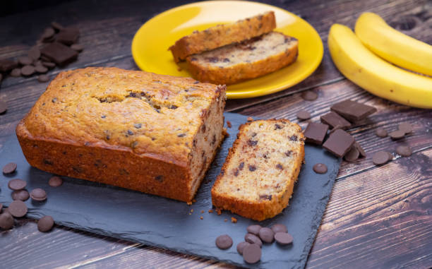 Banana bread on cutting board with chocolate chips Banana bread on cutting board with chocolate chips and fresh banana in background. fruitcake stock pictures, royalty-free photos & images