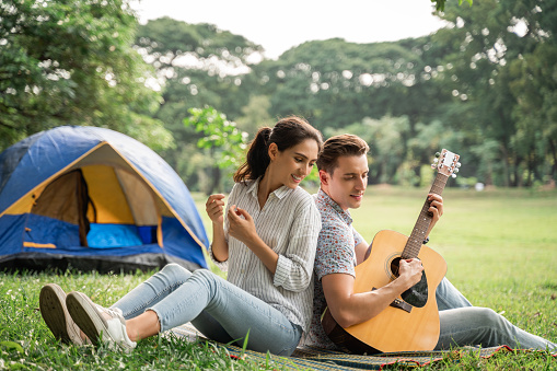 Picnic and Camping time. Young couple having fun with guitar on picnic and Camping in the park. Love and tenderness, Romantic man playing guitar to his girlfriend, lifestyle concept
