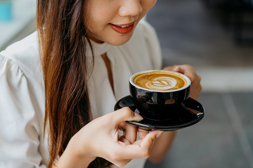 A shot of young asian woman holding a cup of coffee with saucer, enjoying a quiet moment in cafe