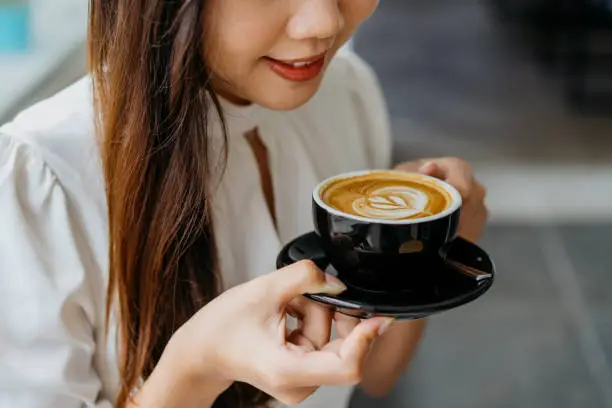 Photo of Young asian woman holding a cup of coffee with saucer