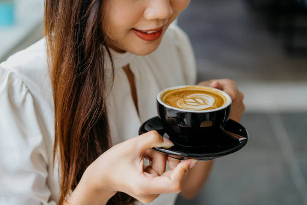 молодая азиатская женщина, держащая чашку кофе с блюдцей - latté cafe froth art cup стоковые фото и изображения