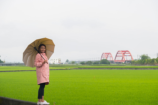 Woman with yellow umbrella standing with with rice filed and red red bridge at yuli Hualien Taiwan background.