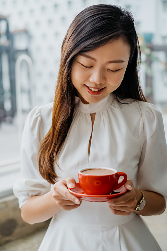 A shot of young asian woman holding red coffee cup and saucer, enjoying a quiet moment in cafe