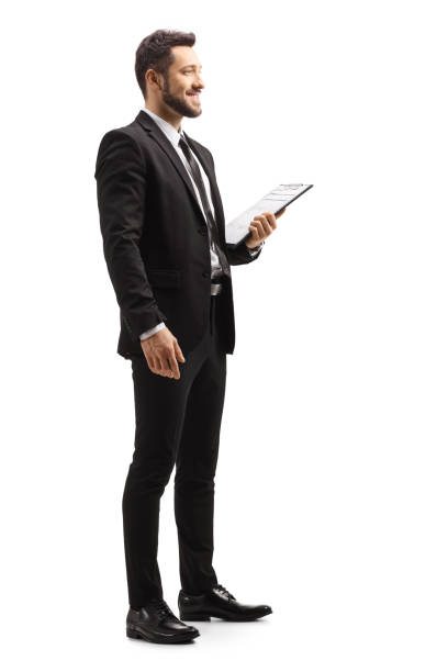 Elegant man in a black suit holding a clipboard Full length profile shot of an elegant man in a black suit holding a clipboard isolated on white background man standing profile stock pictures, royalty-free photos & images