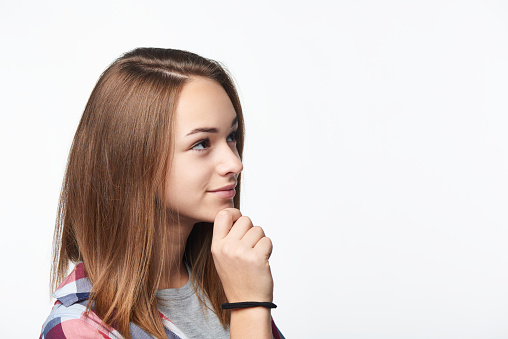 Profile portrait of thinking girl looking forward at blank copy space with hand on chin