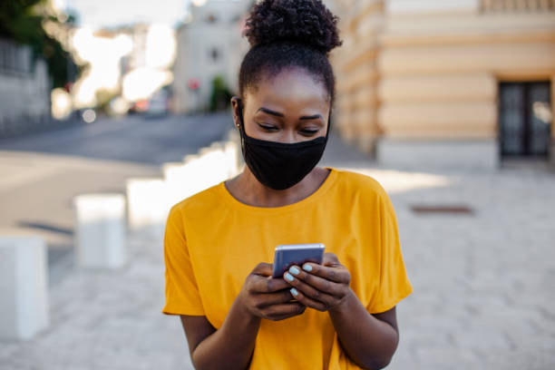 istock Woman with a mask outdoors using smart phone 1264111564