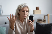 Grandmother holding smartphone looks at device screen feels angry