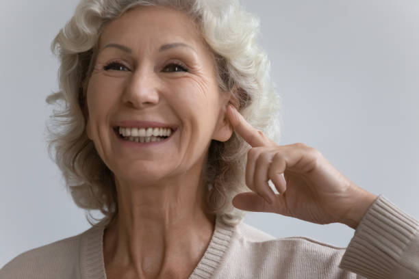 istock Elderly woman points finger to ear with hearing aid device 1264113488