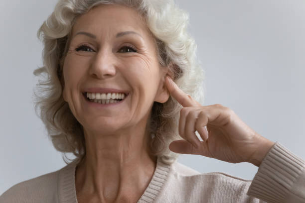 idosa aponta dedo para orelha com aparelho auditivo - aparelho auditivo - fotografias e filmes do acervo