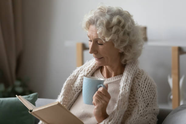 istock 60s woman sitting on sofa drinking tea reading a book 1264113496