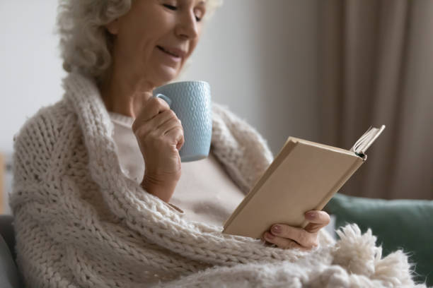 istock Mature woman relaxing on sofa drinking tea reading a book 1264113501