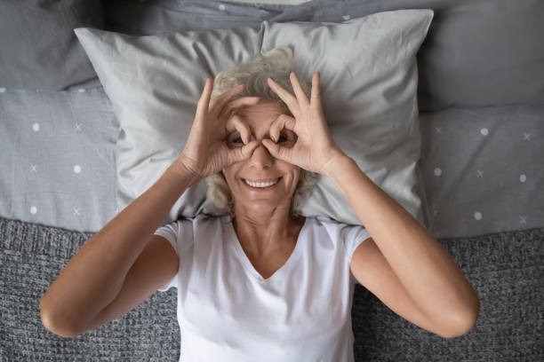 istock Elderly woman lying in bed looking through fingers glasses shape 1264113541