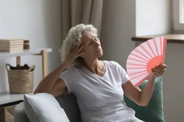 Photo of Senior woman waving fan feels unwell due unbearable hot weather