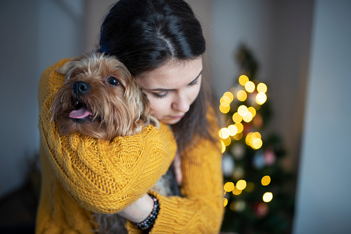 Young female and her dog are cuddling next to the Christmas tree at the background of Christmas light , joyful and warm Christmas holidays