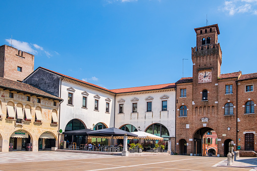 People sitting at the outdoor tables in Piazza Grande, the main square of Oderzo, where overlook the cathedral and the Torresin, one of the historic symbols of the town.