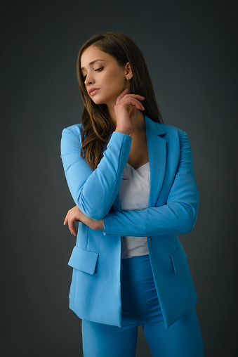 Young female fashion model posing in studio in light blue suit over gray background
