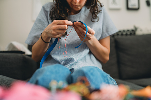 Young woman is sewing a bracelet at home. She's using needle and thread.