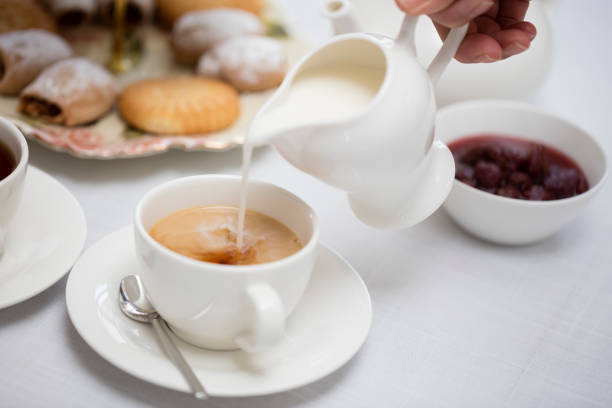 versando latte sul tè inglese caldo in una tazza da tè bianca - tea cakes foto e immagini stock