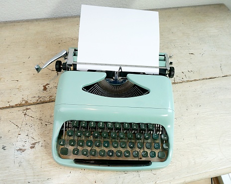 Retro typewriter with blank paper inserted sitting on a desk. The typewriter is a model from the 1960s in Mint Green.