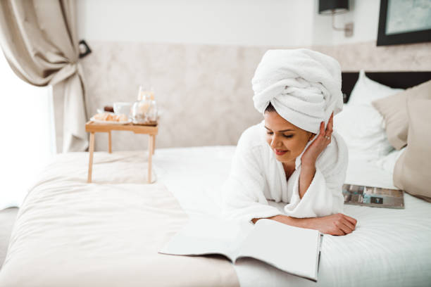 donna che mangia la colazione a letto e legge una rivista - bathrobe women cup towel foto e immagini stock