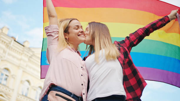 glücklich lieben homosexuell lesbische lgbt paar küssen in der stadt straßen halten regenbogen-flagge - sex symbol couple kissing women stock-fotos und bilder