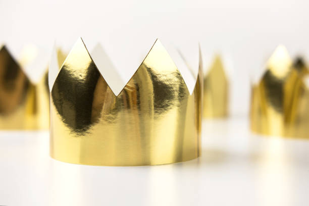 istock Cardboard golden crowns lying on a white table. Minimalistic style. 1264131512