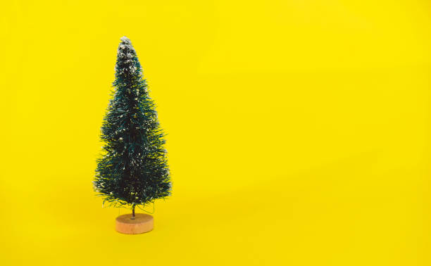 istock Miniature toy artificial Pine tree on wooden base on bright yellow Christmas background with long shadow. Concept of New Year, Christmas holiday greeting card. 1264131563