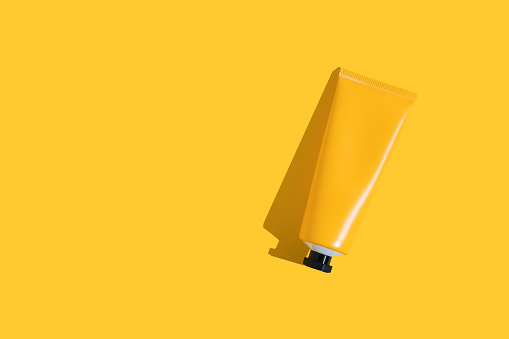 Yellow tube of sunscreen on a bright yellow background with hard shadow. Sun protection in the summer