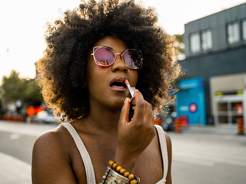 Young African American woman feeling good while adjusting lipstick. Urban exterior in the summer.