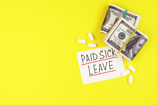 text paid sick leave and money with pills on a yellow background. dollars and medical capsules on the table